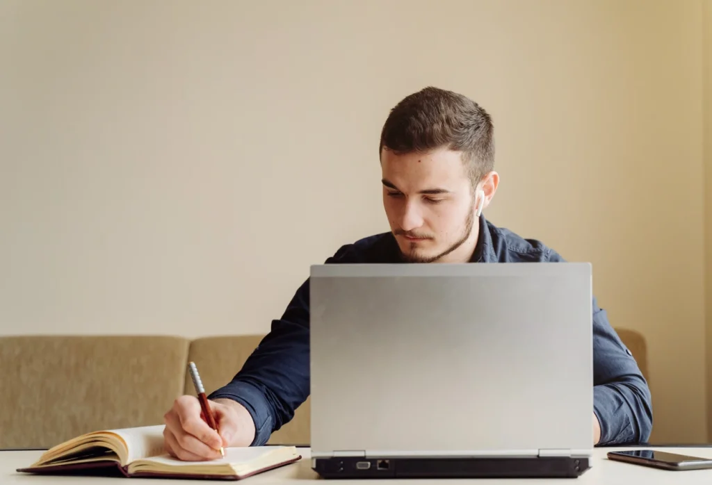 Man studying and writing while using a laptop