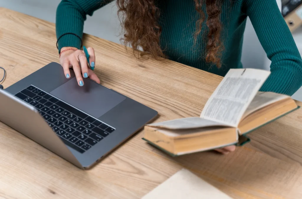 Person using laptop while reading a book