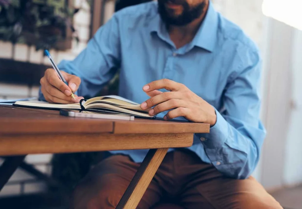 Person writing in a notebook at an outdoor table.